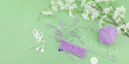 Spring knitting concept. Pattern example, traditional tools, ball of yarn, blooming cherry branch. Creative handmade flat lay, pastel green background, banner format