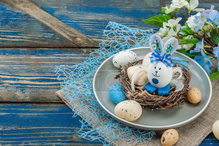 Easter table setting with eggs, bird's nest and blooming branch. Traditional festive symbols, greeting card, flat lay. Old wooden boards background, copy space