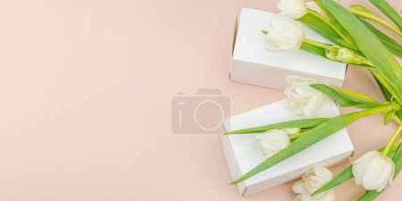 Geschenkkonzept. Eingewickelte Überraschungsschachtel, weiße Tulpen auf Aprikosengrund. Alles Gute zum Geburtstag, Valentinstag oder Muttertag, Hochzeit, Bannerformat