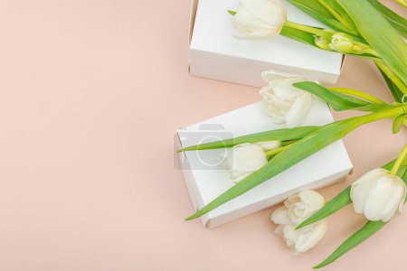 Geschenkkonzept. Eingewickelte Überraschungsschachtel, weiße Tulpen auf Aprikosengrund. Alles Gute zum Geburtstag, Valentinstag oder Muttertag, Hochzeit, Draufsicht