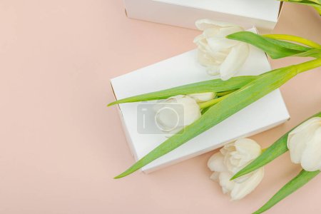 Geschenkkonzept. Eingewickelte Überraschungsschachtel, weiße Tulpen auf Aprikosengrund. Alles Gute zum Geburtstag, Valentinstag oder Muttertag, Hochzeit, Draufsicht