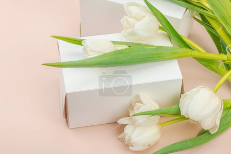 Geschenkkonzept. Eingewickelte Überraschungsschachtel, weiße Tulpen auf Aprikosengrund. Alles Gute zum Geburtstag, Valentinstag oder Muttertag, Hochzeit aus nächster Nähe