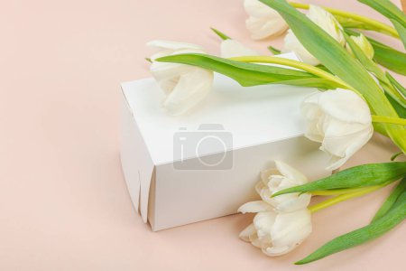 Geschenkkonzept. Eingewickelte Überraschungsschachtel, weiße Tulpen auf Aprikosengrund. Alles Gute zum Geburtstag, Valentinstag oder Muttertag, Hochzeit, Kopierraum