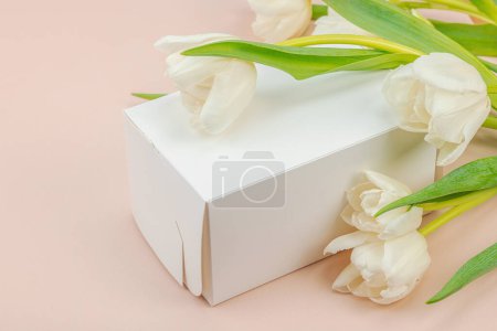 Geschenkkonzept. Eingewickelte Überraschungsschachtel, weiße Tulpen auf Aprikosengrund. Alles Gute zum Geburtstag, Valentinstag oder Muttertag, Hochzeit, Kopierraum