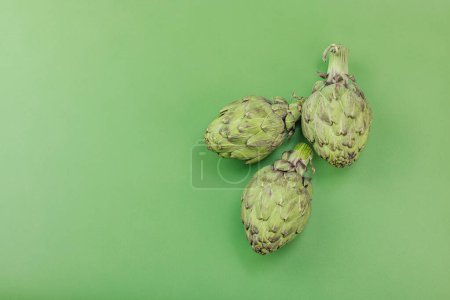 Fresco globo de alcachofa cocinar sobre un fondo verde. Ingredientes tradicionales de temporada para una comida vegana saludable, laico plano, vista superior