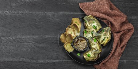 Traditional italian artichoke, cooked carciofi vegetable. Olive oil, garlic, parsley and lemon. Dark wooden background, spicy sauce, close up