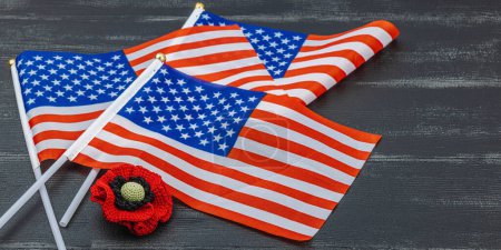 Memory Day concept. United States of America flags and handmade crochet poppy flower. Traditional symbols, flat lay, black wooden background, banner format