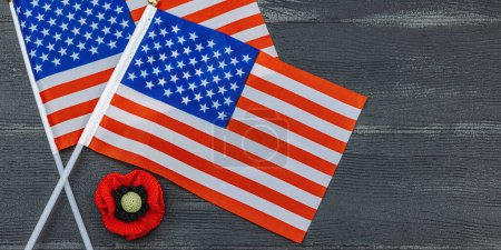 Memory Day concept. United States of America flags and handmade crochet poppy flower. Traditional symbols, flat lay, black wooden background, banner format