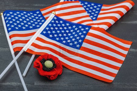 Memory Day concept. United States of America flags and handmade crochet poppy flower. Traditional symbols, flat lay, black wooden background, close up