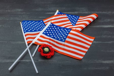 Memory Day concept. United States of America flags and handmade crochet poppy flower. Traditional symbols, flat lay, black wooden background, copy space