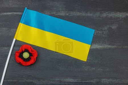 Memory Day concept. Ukrainian flag and handmade crochet poppy flower. Traditional symbols, flat lay, black wooden background, top view