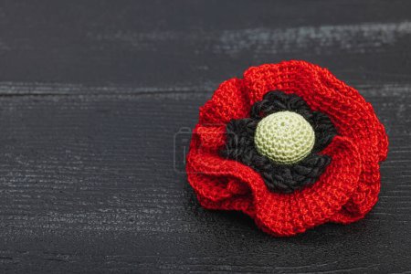 Memory Day concept. Handmade crochet poppy flower. Traditional symbol, flat lay, black wooden background, close up
