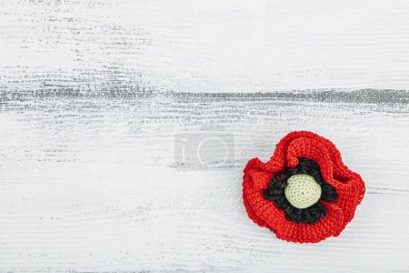 Memory Day concept. Handmade crochet poppy flower. Traditional symbol, flat lay, white wooden background, top view