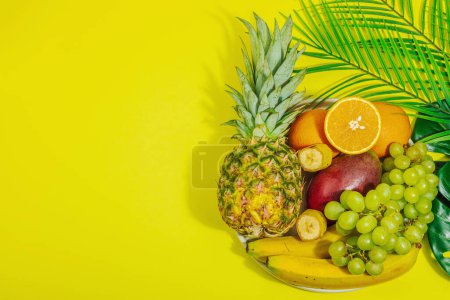 Ensemble de fruits tropicaux frais. Mangues mûres, ananas, oranges, raisins et bananes. Lumière dure, ombre sombre, fond jaune, vue de dessus