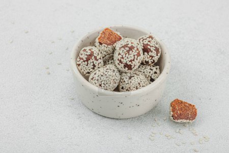 Vegan coconut candies in sesame seeds. Ready to eat food, healthy lifestyle concept. White stone concrete background, copy space