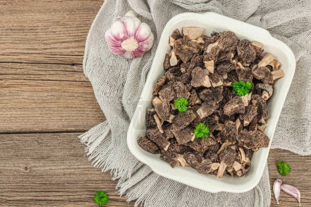Raw black morel mushrooms with fresh parsley. Vegan ingredient for cooking healthy food. Hobby hunter concept, wooden background, top view