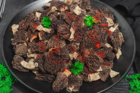 Rohe schwarze Morcheln mit frischer Petersilie. Vegane Zutat zum Kochen gesunder Lebensmittel. Hobby-Jäger-Konzept, schwarzer Holzhintergrund, Nahaufnahme