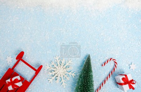 Świąteczna kartka z białymi pudełkami, płatkami śniegu, czerwonymi saniami, cukierkami i choinką. niebieski śnieg tło z przestrzeń kopiowania