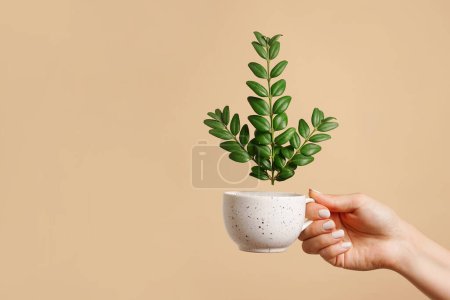 taza de mano con hojas verdes sobre fondo beige, espacio para copiar