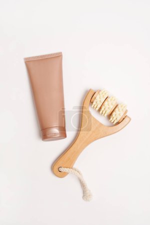 Foto de Rodillo de madera para masaje corporal y crema cosmética o loción en tubo beige, fondo blanco - Imagen libre de derechos