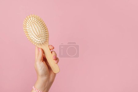 Mano de mujer sosteniendo el cepillo de madera sobre fondo rosa, espacio de copia