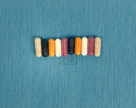 Téléchargez les photos : Top view of a variety of vitamin and mineral supplements in capsules. Multicolored pills in orange and red on blue textured background. - en image libre de droit