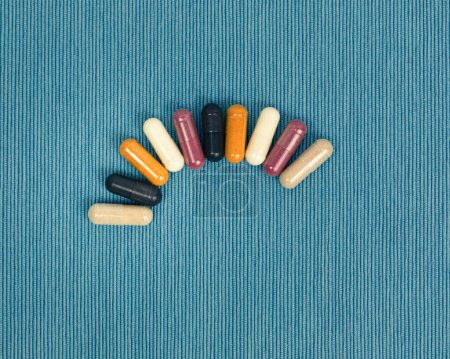 Téléchargez les photos : Top view of a variety of vitamin and mineral supplements in capsules. Multicolored pills in orange and red on a blue textured background. - en image libre de droit