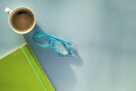 Téléchargez les photos : Une tasse à café du matin, une paire de lunettes de lecture bleues et un vert - en image libre de droit