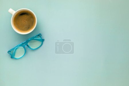 Téléchargez les photos : Une tasse de café du matin et une paire de lunettes de lecture bleues sur un sol - en image libre de droit