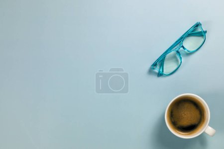 Téléchargez les photos : Une tasse de café du matin et une paire de lunettes de lecture bleues sur un sol - en image libre de droit