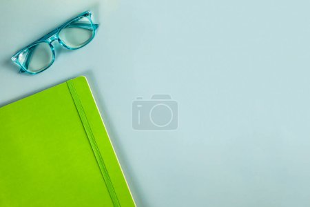 Téléchargez les photos : Une paire de lunettes de lecture bleues et un carnet vert sur un b solide - en image libre de droit