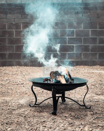 Téléchargez les photos : Fumée provenant d'un feu brûlant dans un foyer de jardin avec du bois - en image libre de droit