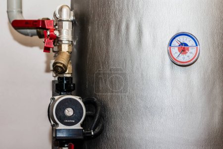 Pump, Storage Tank with Thermometer for Water Heating system at Home. Manometer, Buffer Tank, pipe, Valves of Heat system in Boiler room in House.