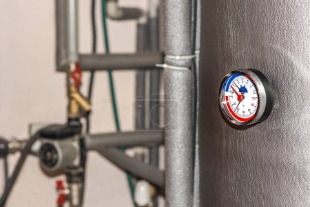 Photo for Boiler Hot Water Storage Tank with Circular Thermometer, Valves, Circulation Pump, Pipes of Water Heating System in House Boiler room. Start of the heating season. Energy crisis. - Royalty Free Image