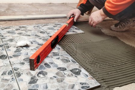 Foto de Laying Floor Ceramic Tile. Construction Worker laying tiles over Concrete Floor using Tile Levelers, notched trowels and tile Mortar. Renovating the floor. - Imagen libre de derechos