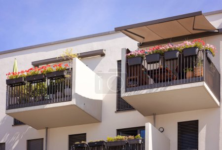 Téléchargez les photos : Balcon de l'immeuble moderne avec pare-soleil protection Auvent Marquise, Fleurs dans les jardinières à Terrase de l'immeuble résidentiel - en image libre de droit