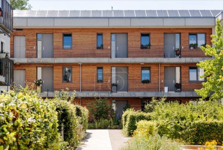 Casa multifamiliar o edificio de apartamentos moderno con panel solar, fachada de madera y paisaje de jardín comunitario está de moda en la construcción urbana en Europa, Alemania. Concepto Eco Vivienda.