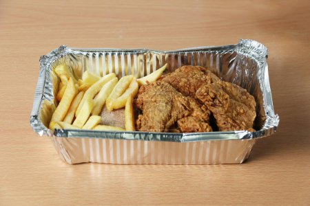 Foto de Comida rápida en un recipiente para llevar de papel de aluminio. Pollo asado y papas fritas - Imagen libre de derechos