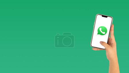 Téléchargez les photos : Main d'une belle femme tenant un téléphone portable avec logo WhatsApp sur fond vert - en image libre de droit