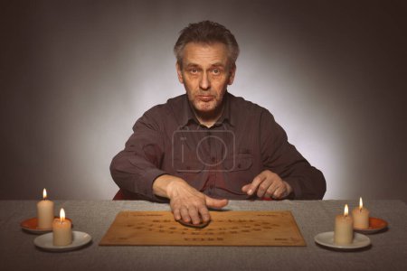 Téléchargez les photos : Spiritiste plus âgé communiquant avec les fantômes à travers ouija - en image libre de droit