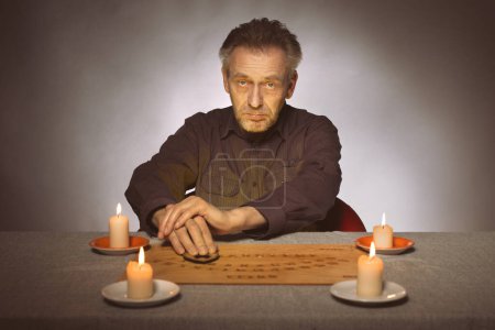 Téléchargez les photos : Spiritiste plus âgé communiquant avec les fantômes à travers ouija - en image libre de droit