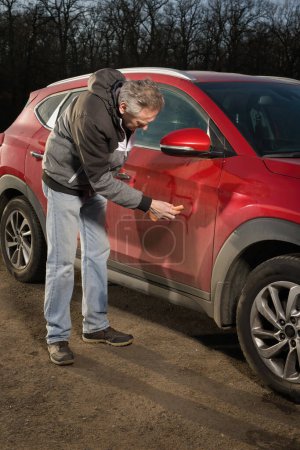 Téléchargez les photos : Homme plus âgé prendre soin annd nettoyage de voiture en plein air sur la nature parking - en image libre de droit