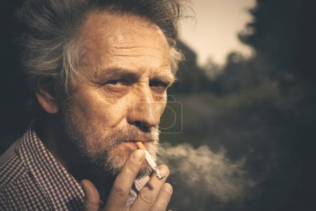 Téléchargez les photos : Homme âgé fumant des cigarettes dans le parc de la ville ces derniers temps le jour - en image libre de droit