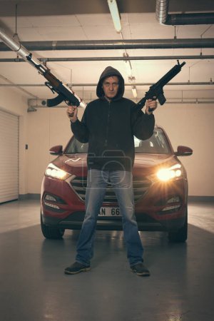 Foto de Hombre con capucha negra armado con pistola automática en busca de un peligro - Imagen libre de derechos