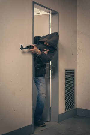Foto de Hombre con capucha negra armado con pistola automática en busca de un peligro - Imagen libre de derechos