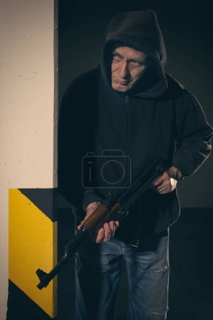 Photo for Man in black hooded shirt armed with automatic gun looking for a danger - Royalty Free Image