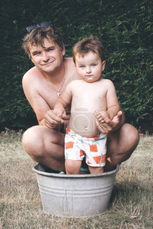 Téléchargez les photos : Père et fils refroidissant dans une petite baignoire en tôle rétro - en image libre de droit