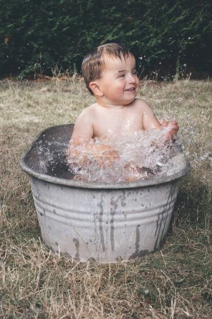 Foto de Niño pequeño que se enfría en una pequeña bañera de chapa retro - Imagen libre de derechos