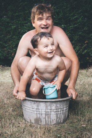 Téléchargez les photos : Père et fils refroidissant dans une petite baignoire en tôle rétro - en image libre de droit