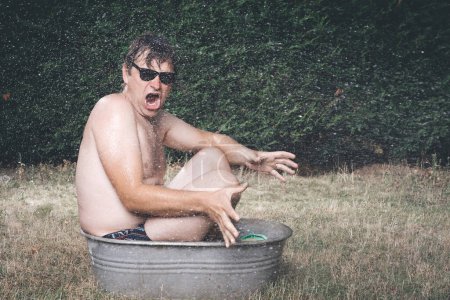 Hombre enfriamiento en bañera de metal retro para niños en verano caliente durante el día